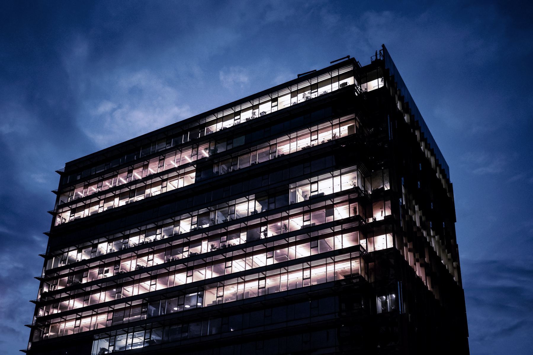 A modern office building at dusk, every floor lit